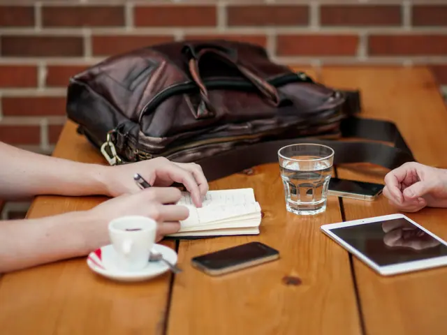 Duas pessoas conversando numa mesa de madeira, com café, caderno de anotações e tablet
